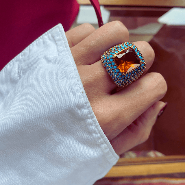 A close-up image of AFET yellow gold plated statement ring with a large central citrine yellow zirconia and turquoise blue zirconia stones on a person's hand.