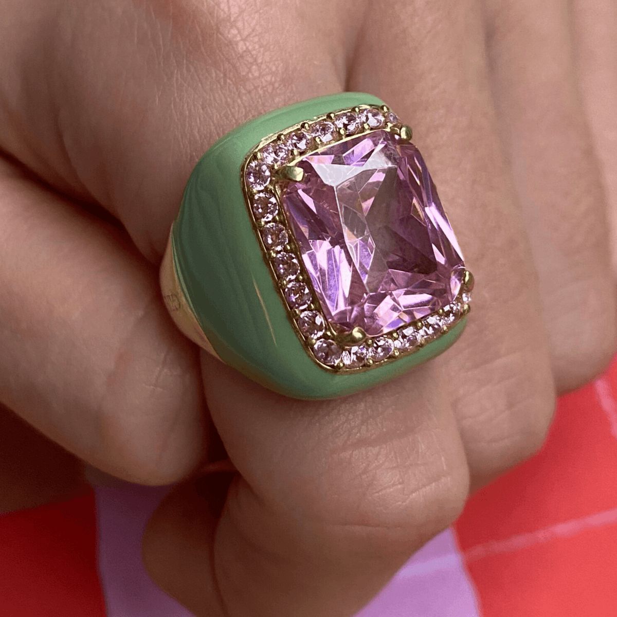 A close-up image of a yellow gold plated ring with pastel green enamel and a large pink zirconia surrounded by smaller pink zirconia stones.