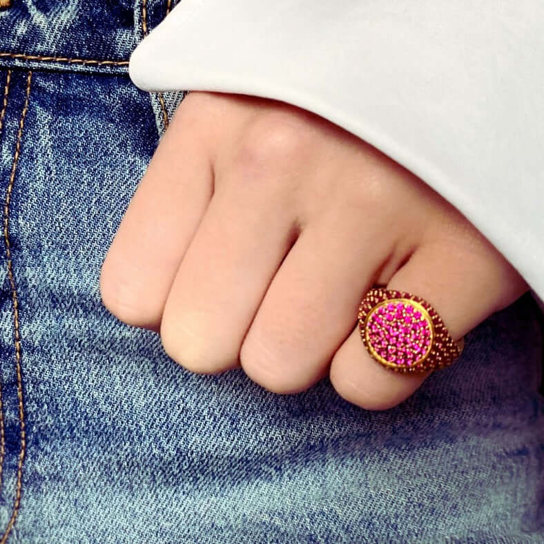 A person's hand wearing a yellow gold plated pinky ring with red zirconias on the top and sides.