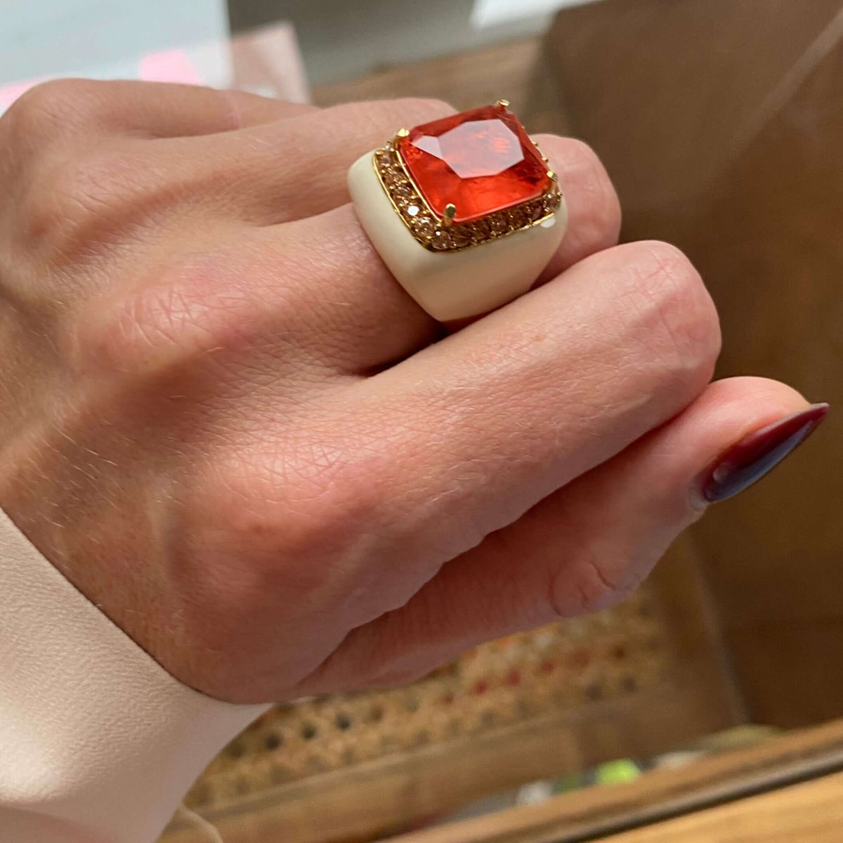 A yellow gold ring with light ivory colored enamel and a large orange doublette surrounded by champagne cubic zirconias displayed on a person's hand.