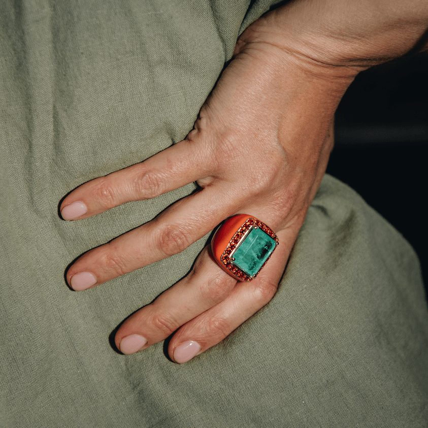 YASMINE'S LITTLE SISTER statement ring, worn on hand, editorial lifestyle view. Salmon enamel band with Aqua green large center stone and orange zirconia halo. GIADAN for Le.Paul Jewelgarden