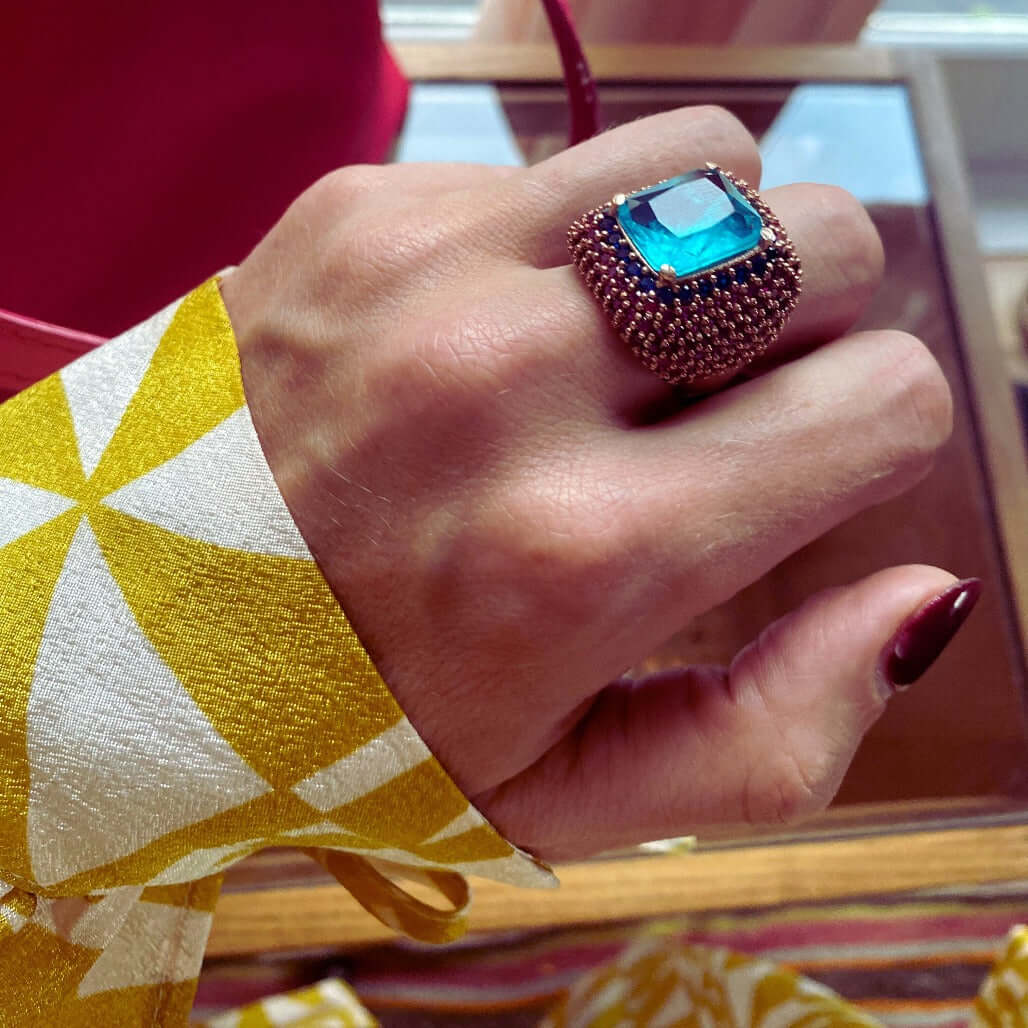 MALIKA cocktail ring on hand showing blue center stone combined with red and dark blue zirconias, bold 22mm width and rose gold setting